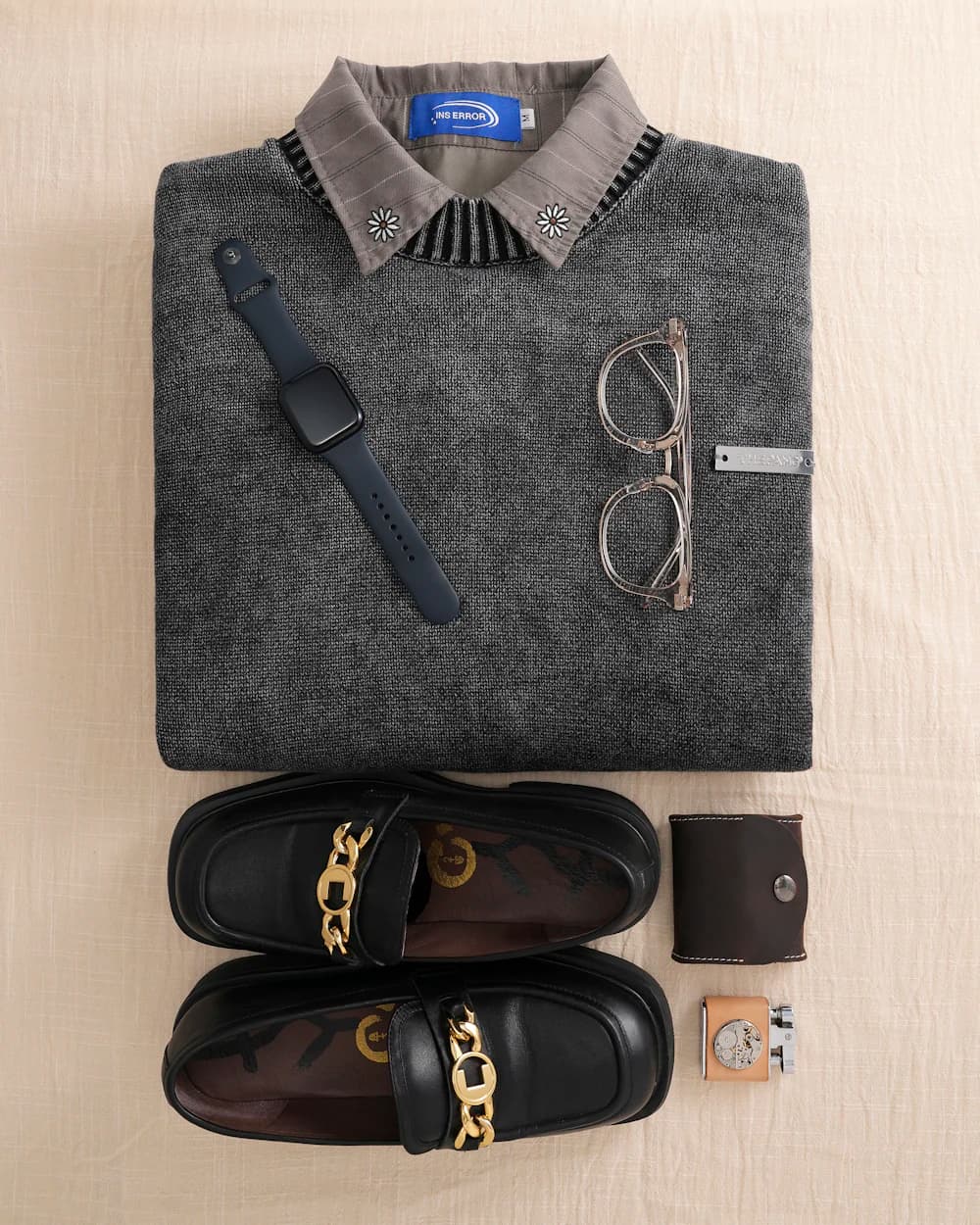 Flat lay of a knit sweater, collared shirt, loafers, glasses, and a wristwatch.