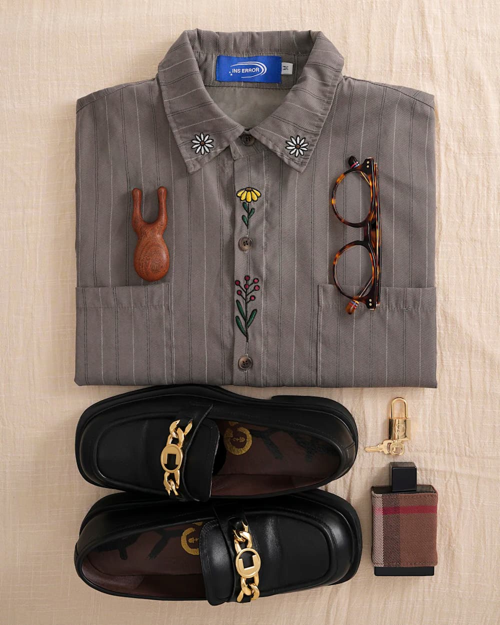 Flat lay of a striped shirt, chain loafers, eyeglasses, and a perfume bottle.